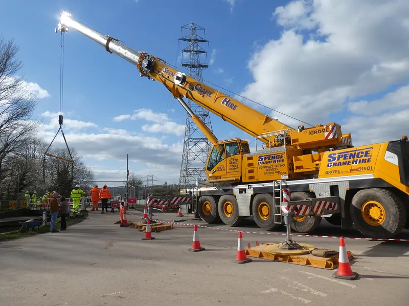 Mobile crane lifting a steel footbridge onto dry land